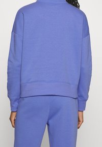 Sudadera de algodón morada con un corte relajado, puños y dobladillo acanalados, y una textura suave. Diseñada con un cuello redondo y mangas largas.