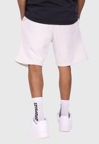 Hvide bomulds-shorts med en afslappet pasform, der har en elastisk talje. Sættes sammen med hvide sneakers og ribbede sokker med sort tekst.