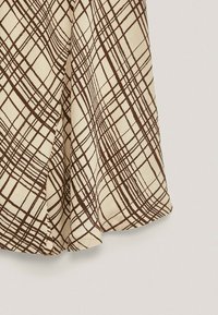 Brown plaid pattern on a cream fabric, featuring intersecting lines. The fabric is smooth with a slight sheen, draping softly.