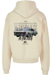 Beige Kapuzenpullover mit einem grafischen Druck eines klassischen Autos, versehen mit dem Text "M. Gonzalez" und "In tha hood" in kontrastierendem Schwarz und Grau.