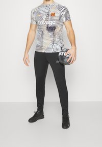 Nike sportswear set featuring a graphic short-sleeve top with abstract patterns in black and white, paired with black elasticated joggers.