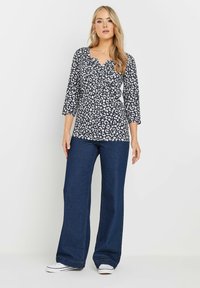 Top leopard in bianco e nero con scollatura a V e maniche a tre quarti, abbinato a jeans svasati blu scuro e sneakers bianche.