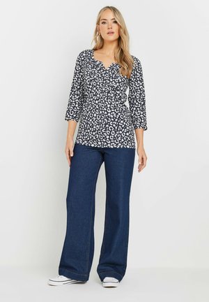 Sort-hvid leopardprint top med V-hals og trekvartærmer, kombineret med mørkeblå flared jeans og hvide sneakers.