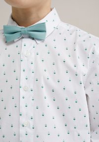 Camicia bianca con piccoli motivi turchesi e verdi che ricordano tazze, dotata di un papillon turchese abbinato e bottoni bianchi lucidi.