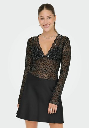 Zwart kanten bodysuit met lange mouwen en een scalloped halslijn, gecombineerd met een zwarte A-lijn rok. Het kant heeft bloemmotieven en een textuurdetail.