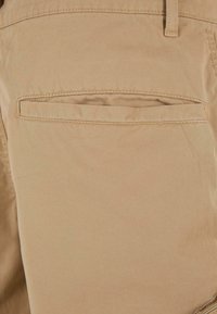 Shorts en coton beige avec une poche arrière à ouverture droite et des détails de couture subtils, mettant en valeur une texture lisse.