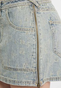 Jasnoniebieska jeansowa spódniczka mini o teksturowanym wykończeniu, z widocznym zamkiem po boku oraz tradycyjnymi kieszeniami.