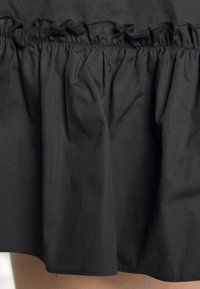 Saia preta com detalhes de babados em camadas e cintura franzida. Tecido liso com acabamento mate, comprimento até ao joelho e costura limpa.