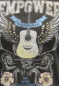 Svart grafisk t-shirt med en akustisk gitarr, vingar och textelement i gult, blått och vitt. Blomstermotiv i botten.