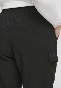 Čierne cargo nohavice s elastickým pásom. Obsahujú bočnú vrecko, hladkú textúru a voľný strih. Detailný pohľad zozadu.