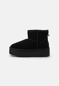 Botas de tobillo negras de ante con suela plana. Presentan una puntera redonda, costuras sencillas y una lengüeta trasera para facilitar su colocación.