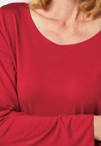 Rotes Langarmoberteil mit großzügigem Rundhalsausschnitt, aus weichem, glattem Material gefertigt. Verfügt über eine entspannte Passform und dezente Nähte entlang der Kanten.
