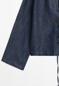 Manche de veste en denim à coupe large et droite avec des coutures visibles, comportant un détail lacé le long de la couture latérale droite.