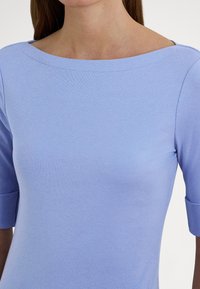 Svetlomodrý krátky rukáv s širokým výstrihom, vyrobený z mäkkého materiálu, s priliehavým strihom a rebrovanou textúrou.