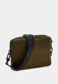 Borsa a tracolla in nylon verde oliva con tracolla nera regolabile, chiusura a zip e design rettangolare minimalista. Presenta dettagli in metallo.