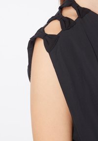 Primer plano del hombro de una blusa sin mangas negra con tres lazos decorativos de tela a lo largo de la tira del hombro.