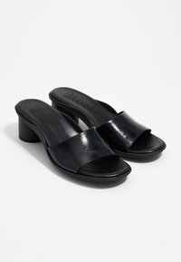 Ein Paar schwarze, offene, Absatz-Slip-On-Sandalen mit breiten Riemen und runden Blockabsätzen auf einem schlichten weißen Hintergrund.