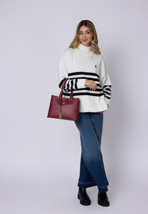 Maglione bianco oversize con strisce nere, abbinato a jeans a gamba larga blu e una borsa tote bordeaux con dettagli dorati.