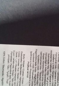 Witte stoffen label met zwarte tekst, met zorginstructies en productdetails in meerdere talen. 100% katoen.