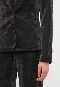Fekete zakó fényes szállal, slim fit szabással, kihajtott gallérral, két elülső zsebbel, egysoros gombolással, texturált anyagból a kifinomult megjelenésért.
