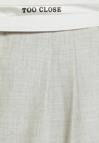 Light gray fabric with a textured surface, featuring a white satin waistband labeled "TOO CLOSE." The fabric has a subtle pattern.