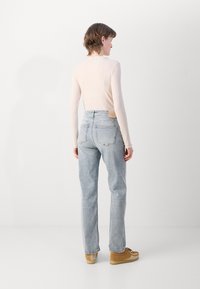 Jeans alto in vita di un blu chiaro con una vestibilità rilassata, sfumature subtle, toppa sulla cintura posteriore, abbinati a calzature beige e una maglietta beige.
