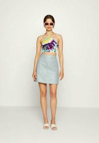 Top cropped em tie-dye multicolor com alças halter, combinado com uma saia mini A-line azul clara e sandálias brancas tipo slide.