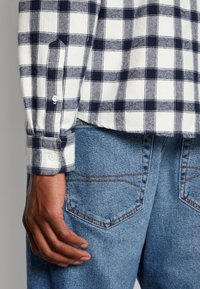 Camicia a quadri con motivo a riquadri navy e bianco, maniche lunghe con polsini a bottone, abbinata a jeans in denim blu chiaro con tasche posteriori.
