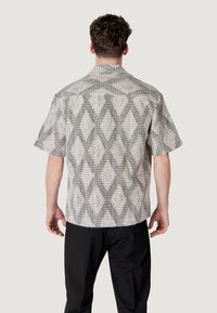 Camicetta a maniche corte in tessuto leggero con un motivo geometrico a diamante in bianco e nero. Design con colletto e taglio dritto.