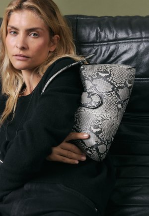 Snakeskin-patterned handbag in gray and black leather, featuring a structured design and a single shoulder strap, held against a black sweater.