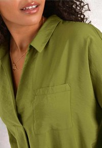 Olive green button-up shirt with a collar and a single chest pocket. Smooth texture, relaxed fit, and lightweight fabric.