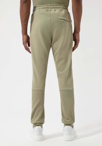 Lichtgroene joggers met een elastische tailleband en een achterzak, voorzien van een soepele textuur en taps toelopende pijpen, gecombineerd met witte sneakers.