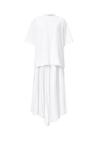 T-shirt blanc à manches courtes associé à une jupe midi blanche plissée asymétrique sur fond blanc uni.