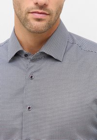 Camicia a maniche lunghe con pattern a quadretti neri e bianchi, colletto standard e bottoni scuri. Realizzata in tessuto a trama con una texture liscia.