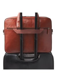 Borsa per laptop in pelle marrone con doppio manico e tasca con zip, attaccata a una valigia nera su ruote con manici in metallo.