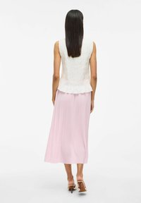 Top bianco strutturato con orlo peplum abbinato a una lunga gonna plissettata rosa chiaro e sandali con tacco beige.