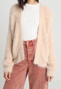 Faux fur cardigan in light beige with long sleeves, open front, and soft texture, paired with high-waisted, faded pink jeans.