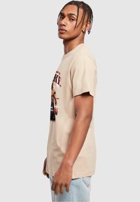 Tricou din bumbac bej cu un imprimeu grafic al unui boxer. Croi standard, mâneci scurte și guler rotund. Text în culori contrastante.