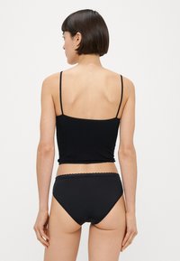 Top court noir à fines bretelles, avec un motif côtelé texturé. Associé à un bas de bikini taille haute assorti, en tissu lisse.