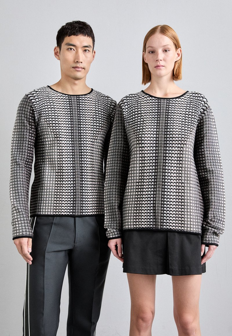 Jerséis de punto con un patrón texturizado en negro y gris, de mangas largas y cuellos redondos, combinados con pantalones grises y una falda negra.