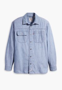 Chemise en denim bleu clair à manches longues, avec deux poches poitrine, fermeture à boutons et col. Le tissu présente un aspect doux et texturé.