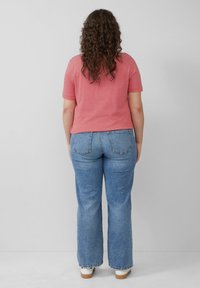 Rood-wit gestreepte top met korte mouwen, gecombineerd met blauwe flared jeans. De top heeft een relaxed fit; de jeans hebben achterzakken en uitgerafelde randen.