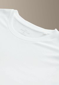 Biele tričko s okrúhlym výstrihom, vyrobené z hladkej bavlny. Má štítok potlačený sivou farbou s názvom značky, veľkosťou a krajinou pôvodu.