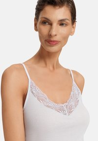 Bílá tílko s krajkovým lemem kolem výstřihu. Nastavitelné ramínka. Měkký materiál a přiléhavý střih.