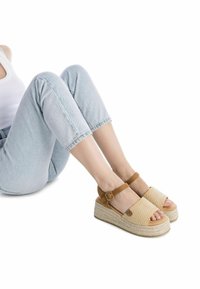 Sandalias de cuña con una correa de ante color tostado y parte superior de tejido beige trenzado. La suela de plataforma con textura de cuerda añade altura. Diseño de punta abierta.