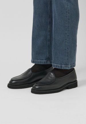 Black leather loafers with a textured upper, rounded toe, and low rubber sole, paired with loose blue denim jeans.