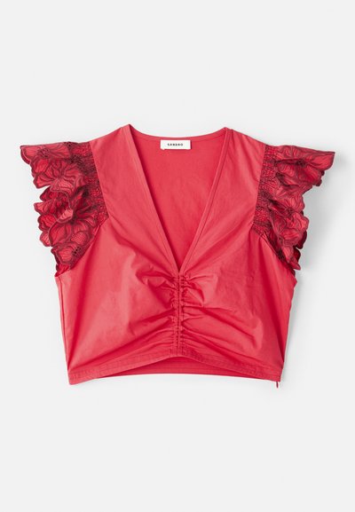 Rød crop top med dyp V-hals, samlet midtdel og korte volangermer med svarte blonder av blomsterdesign. Glatt stofftekstur.