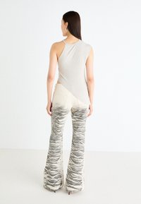 Light gray sleeveless top with an asymmetrical hem, paired with cream flared pants featuring a textured, wavy gray pattern.