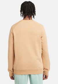 Orange sweatshirt med ribbede mansjetter og kant, blød tekstur, rund halsudskæring og raglanærmer, båret over lysegrønne bukser.