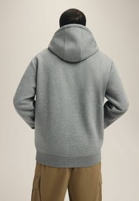 Szara bluza z kapturem o teksturowanym wykończeniu, z dużym kapturem, ściągaczami przy rękawach i dolnej części. Prosty, czysty design bez widocznych logo.